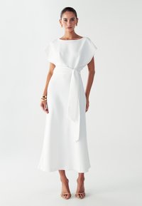 Bijela, lepršava haljina s bočnim izrezom i kratkim rukavima. Povezana u struku s odgovarajućom trakicom. Glatka tekstura, dužine do članka.