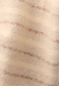 Lana beige chiaro e morbida con una finitura texturizzata, caratterizzata da sottili striature marroni che scorrono orizzontalmente attraverso il tessuto.