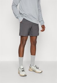 Gray athletic shorts with side slits, paired with a light gray long-sleeve shirt and gray socks. White and beige running shoes complete the outfit.