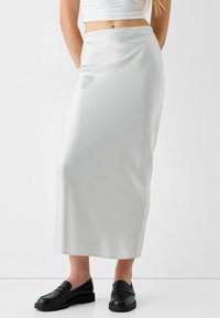 Bílá saténová maxi sukně s hladkou texturou, vypasovaným pasem a postranními kapsami, doplněná černými loafers s texturovaným vzorem.