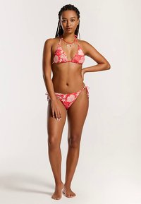 Punane lillemusteriga bikiin, millel on kolmnurga-kujuline top, kaela ümber seotud paeladega ja alumisel osal reguleeritavad küljele paelad; sile ja veniv kangas.