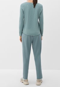 Helles blaugraues Langarmhemd mit abgerundetem Saum, kombiniert mit passenden schmal zulaufenden Hosen. Strukturierter Stoff und bequemer Schnitt, getragen mit beigen Sneakern.