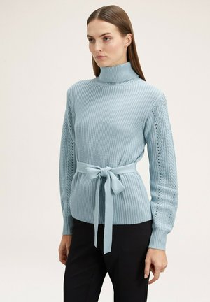 Suéter de punto azul claro con cuello alto y textura acanalada. Presenta un cinturón atado en la cintura y mangas detalladas con un patrón de ojetes.