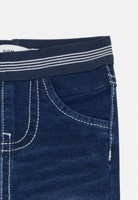 Mörkblå denimjeans med en texturerad yta, vit kontrasterande sömnad, en framficka och ett ribbat midjeband med vita ränder.