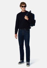Suéter de punto navy, con acentos en color rojo en el cuello, jeans de mezclilla azules, zapatillas gris, gafas de sol negras y una mochila azul. Un conjunto simple y casual.