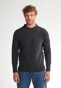 Pull noir en maille avec un col et des poignets côtelés, manches longues et design ajusté, associé à un jean bleu. Tissu en tricot texturé.