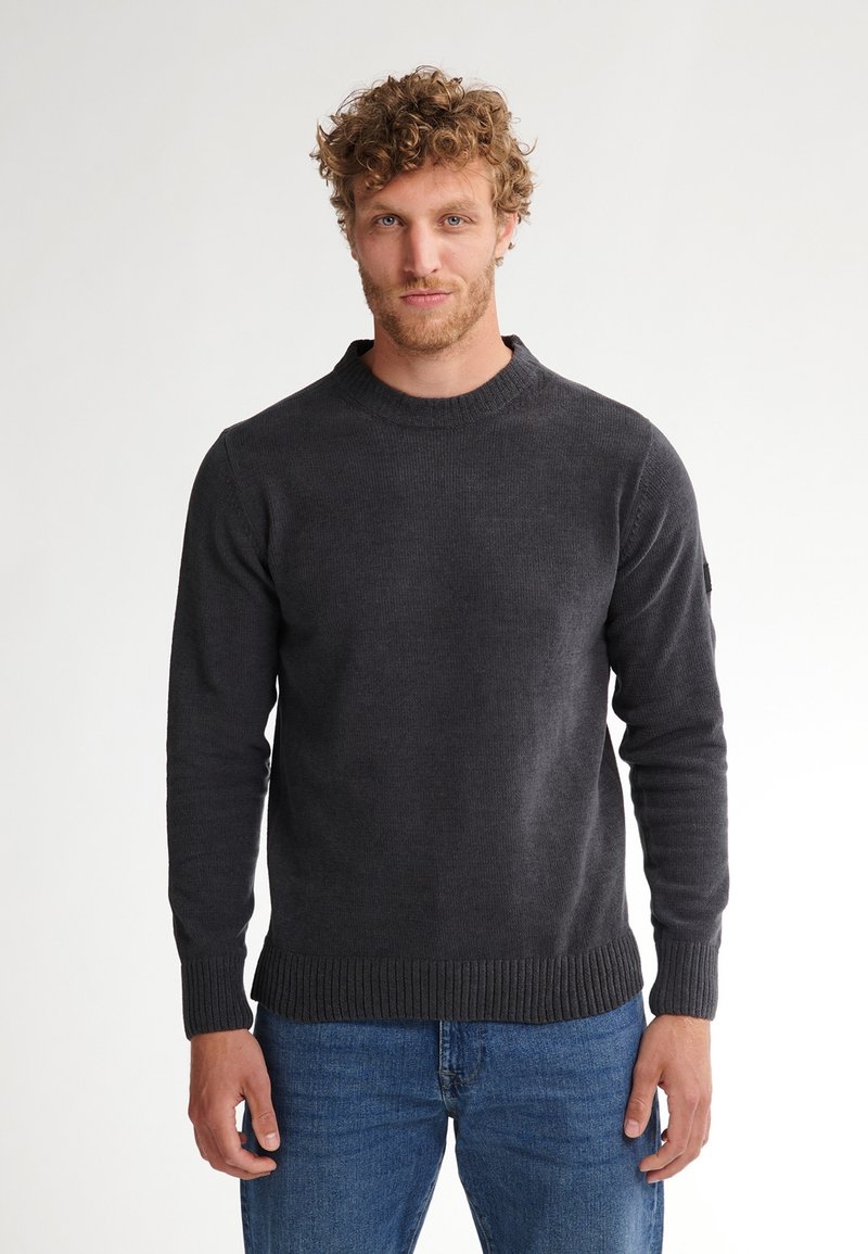Pull noir en maille avec un col et des poignets côtelés, manches longues et design ajusté, associé à un jean bleu. Tissu en tricot texturé.