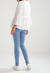Weißes, locker sitzendes Peplum-Top mit dreiviertellangen Glockenärmeln, kombiniert mit hellblauen Skinny-Jeans und weißen Turnschuhen.