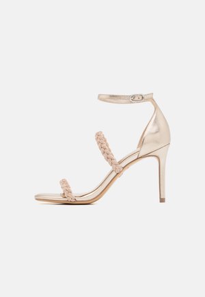 Sandale à talon haut en métal doré avec trois sangles tressées, boucle à la cheville et un talon mince. Texture lisse avec une finition brillante.