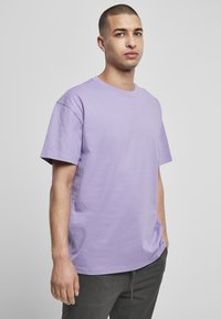 Tricou cu mânecă scurtă și guler rotund, de culoare lavandă deschisă, realizat din bumbac moale, cu o croială lejeră și cusături plate. Fără modele sau accente vizibile.