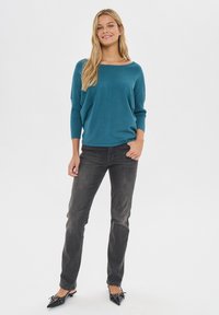 Maglione turchese lavorato a maglia con scollo ampio e maniche a tre quarti abbinato a jeans slim-fit grigio scuro e scarpe nere a punta.