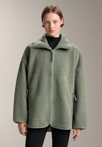 Groene fleecejack met een ritssluiting aan de voorkant, hoge kraag en zijzakken met rits. Zacht, gestructureerd materiaal en een losse pasvorm.