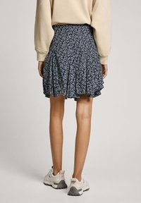 Gonna blu navy a fiori con pieghe, caratterizzata da un orlo arricciato. Indossata con sneaker di colore chiaro. Tessuto morbido con una vestibilità comoda.