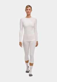 Witte, langärmeliges baselayer-top en legging gemaakt van een glad, rekbaar materiaal; nauwsluitend ontwerp in een naadloze stijl met minimale merkuitingen.