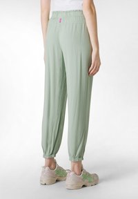 Pantalones sueltos de color verde claro cuentan con una cintura elástica y puños fruncidos, confeccionados con una tela suave de textura lisa.