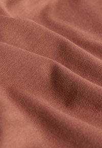 Kopparfärgat tyg med en mjuk, texturerad yta som visar subtila vågor och veck. Materialet ser slätt och välvävt ut.