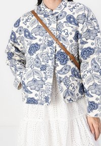 Kurtka pikowana w kolorze kremowym z niebieskim wzorem kwiatowym, z kołnierzem, zapięciem na guziki i bocznymi kieszeniami. Dołączony brązowy pasek na ramię.