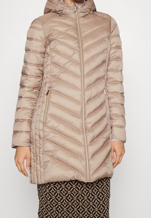 Woman wearing a beige quilted hooded jacket with diagonal stitching and zippered side pockets.