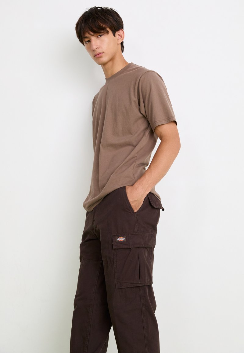 T-shirt en coton marron avec un col rond, associé à un pantalon cargo marron foncé doté de poches latérales et d'un patch logo sur la jambe.