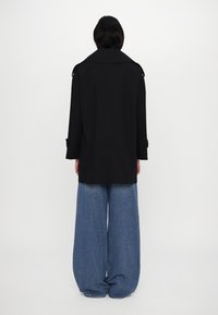 Černá oversized bunda s širokým límcem, dlouhými rukávy a detaily na knoflíky, spárovaná s volnými, světle modrými džíny s vysokým pasem.