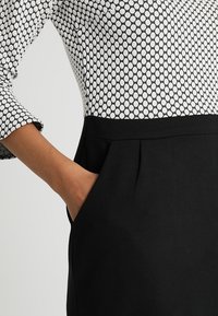 Robe noire avec une silhouette ajustée présentant un haut à motifs noir et blanc. Manches longues et une poche latérale sur le côté de la jupe.