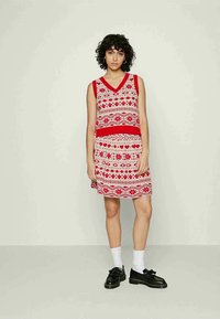 Vestido vermelho sem mangas com decote em V, apresentando um padrão geométrico e floral branco, faixa sólida vermelha na cintura e comprimento acima do joelho.