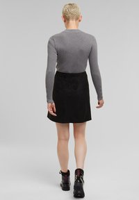 Grijze gebreide lange mouw top met knoopaccenten, gecombineerd met een zwarte suède minirok en zwarte enkellaarsjes met een rode accent.