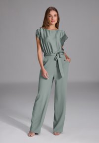 Jumpsuit verde in satin con gambe larghe, maniche corte e vita con cintura. Caratterizzato da tasche laterali e una trama morbida e fluida.
