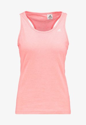 Femme en haut sans manches rose, pantalon de jogging noir et baskets blanches marchant ou faisant du jogging sur un fond clair uni.