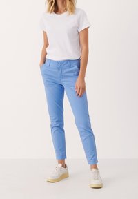 Chinos bleu clair en coton, de coupe slim, avec poches latérales et ourlet retroussé, associés à un t-shirt blanc basique et des baskets.