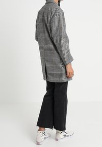 Svartvitt hundtandsmönstrad lång skjortjacka, kombinerad med svarta vida byxor och vita höga sneakers.