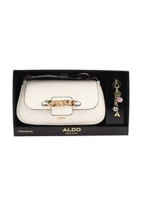 Biała torebka z eko skóry z złotymi elementami i tłoczonym wzorem logo, zawiera breloczek z zawieszkami i wzorem kostki do gry, zapakowana w czarne pudełko.