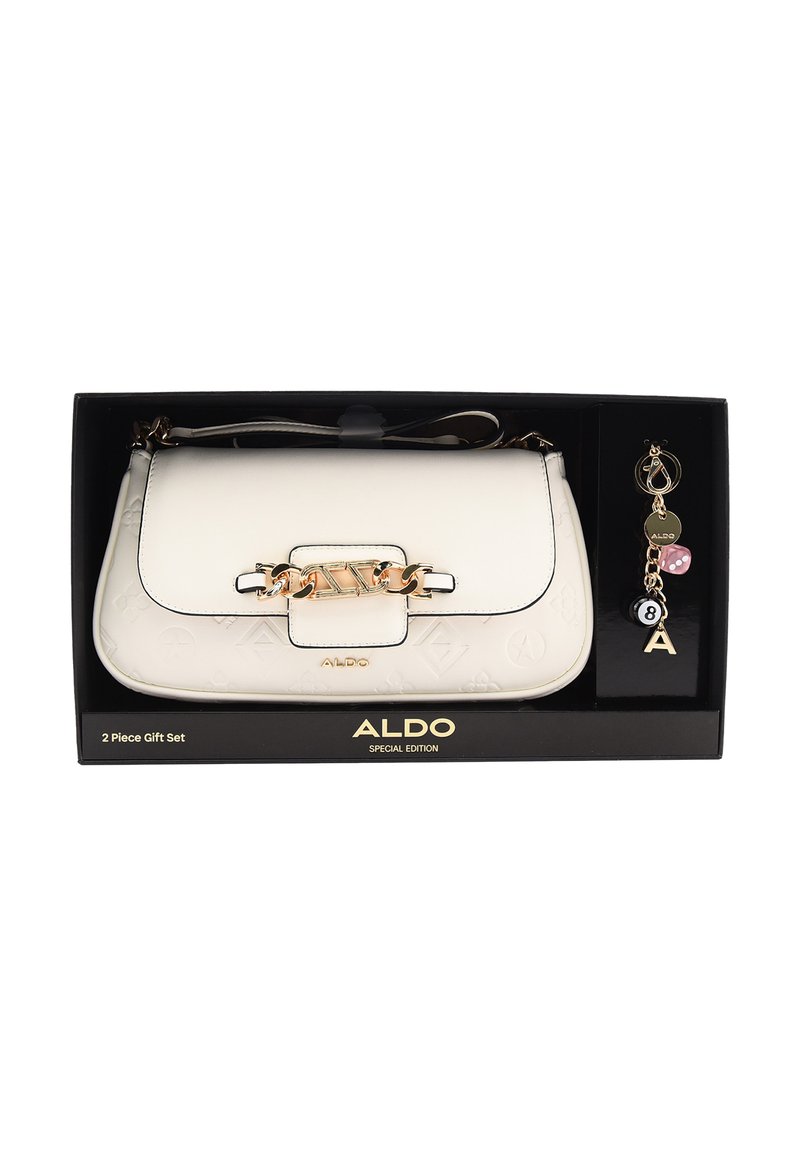 Biała torebka z eko skóry z złotymi elementami i tłoczonym wzorem logo, zawiera breloczek z zawieszkami i wzorem kostki do gry, zapakowana w czarne pudełko.