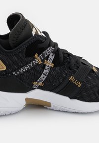 Černá sportovní bota s síťovinovým svrškem, zlatými akcenty, bílou podrážkou a charakteristickým páskem se grafikou "PROČ NE ZERO".