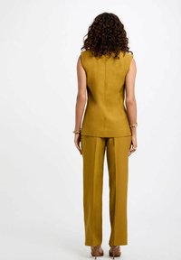 Top sin mangas de color mostaza ajustado, combinado con pantalones rectos; presenta líneas limpias y una textura suave. Diseño simple.