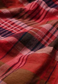 Roter und brauner Karostoff mit weicher Textur, der verschiedene Quadrate in Schattierungen von Rot, Rosa und Dunkelblau mit feinen gewebten Linien zeigt.