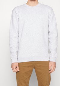 Sweat-shirt gris en coton avec un col rond, des manches longues et des poignets côtelés. Présente un détail de logo subtil sur la poitrine. Se porte avec un pantalon kaki.