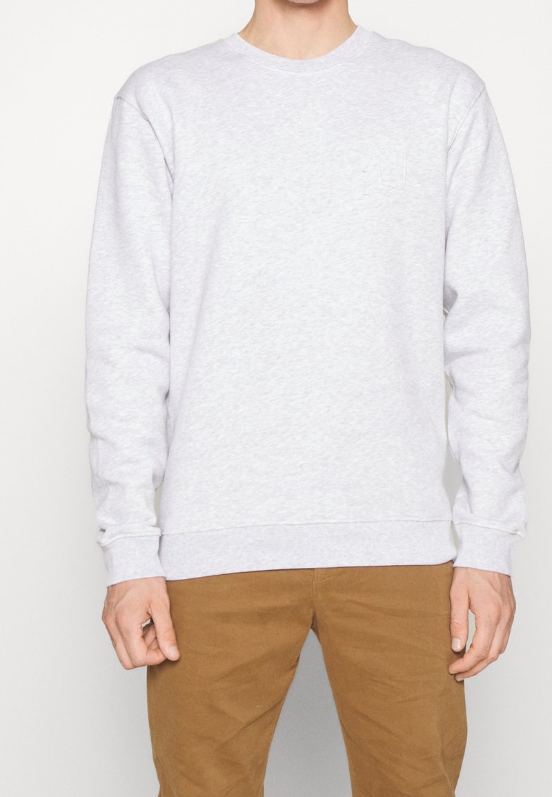 Sweat-shirt gris en coton avec un col rond, des manches longues et des poignets côtelés. Présente un détail de logo subtil sur la poitrine. Se porte avec un pantalon kaki.