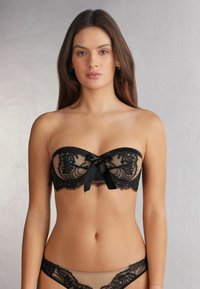 Black lace strapless bra with scalloped edges and a satin bow at the center. Coordinating sheer black lace panties complete the look.