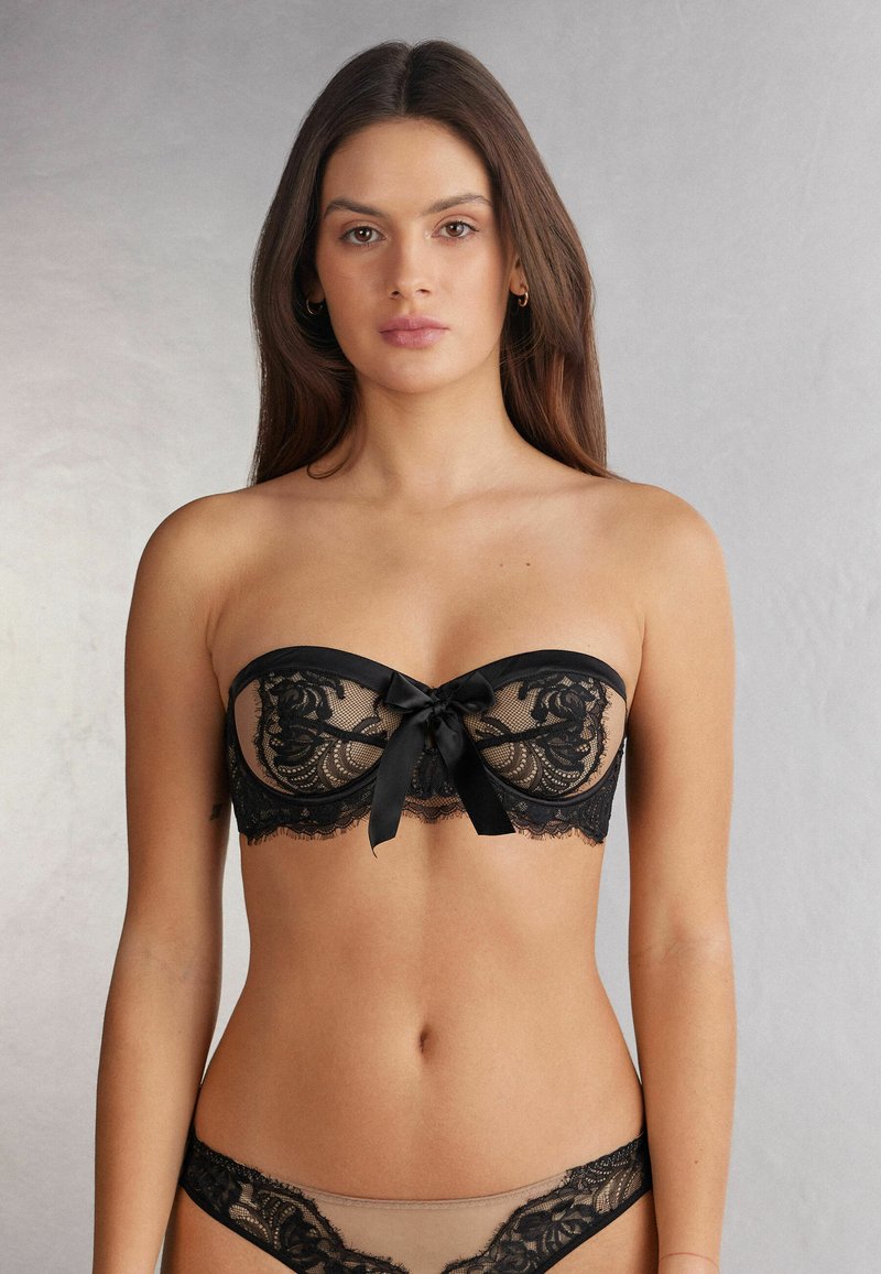 Black lace strapless bra with scalloped edges and a satin bow at the center. Coordinating sheer black lace panties complete the look.