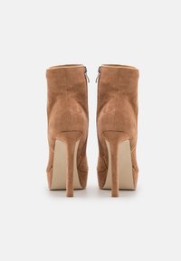 Bottes chevilles en daim marron avec un bout pointu, une fermeture éclair au dos et un talon stiletto haut. Texture lisse et détails de couture minimalistes.