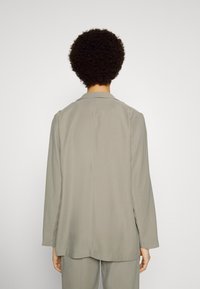 Blazer cinza claro com um colarinho estruturado, mangas longas e uma textura suave. Apresenta um corte reto e um design minimalista.