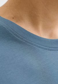 Hele sinine puuvillane T-särk ümmarguse ribaga kaelusega. Kangas on sileda tekstuuriga. Kaeluse ääres on nähtavad õmblused.