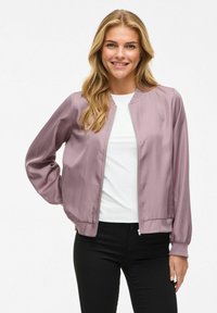 Giacca bomber in satin viola chiaro con zip davanti, polsini e orlo a costina, abbinata a una camicia bianca e pantaloni neri.