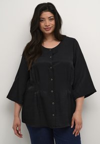 Blusa negra con escote redondo, mangas cortas y anchas, y cierre frontal de botones. La tela tiene una textura suave con un ligero brillo.