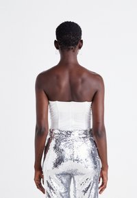 Haut blanc sans bretelles avec un design structuré, associé à un pantalon en sequins argentés taille haute, mettant en valeur une texture lisse et une brillance.