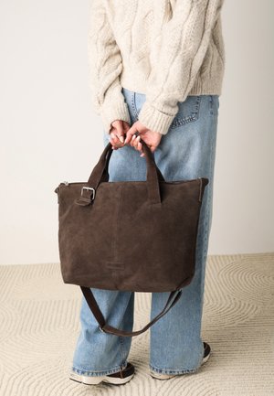 Sac tote en daim marron avec des poignées courtes et une bandoulière réglable. Fermeture à glissière et détail de logo à l'avant. Surface texturée.