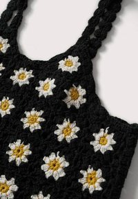 Sac noir en crochet orné d'une broderie de marguerites blanches et jaunes, avec des lanières tressées et une surface texturée.