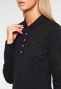Schwarzes Langarm-Polohemd mit Kragen, ausgestattet mit einer Knopfreihe, strukturiertem Stoff und einem kleinen Logo auf der linken Brust.