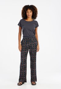 Graues Kurzarmoberteil kombiniert mit weitgeschnittenen schwarzen Hosen mit floralem Muster, die blaue, rosa und weiße Akzente aufweisen. Schmaler Schnitt, legere Stil.